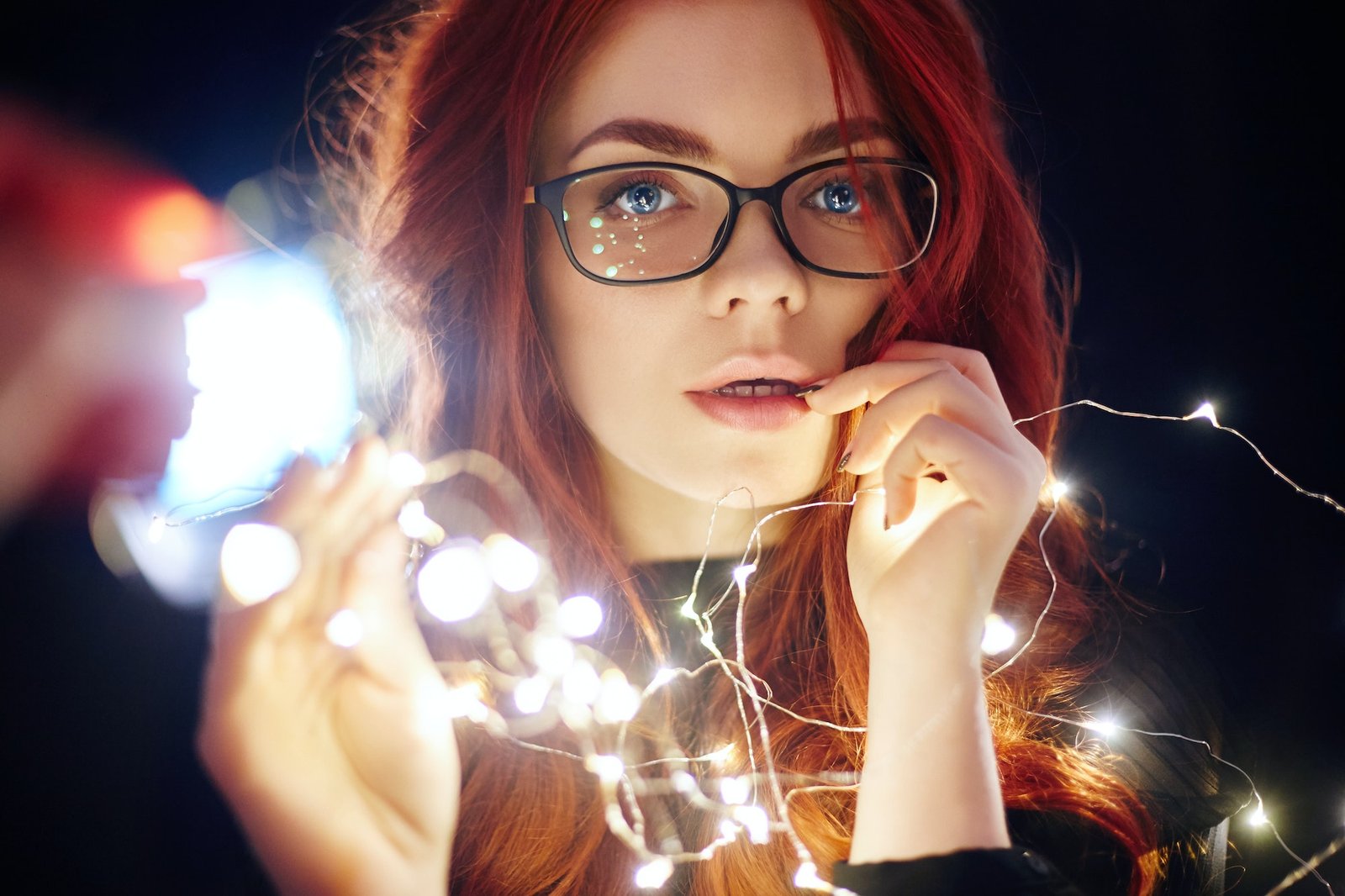 Art portrait of a woman with red hair in Christmas lights. Girl in glasses with reflected Christmas