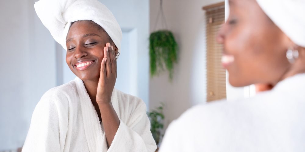 Skincare, face and cosmetic cream of an African woman using facial beauty products for morning self care. Female with a smile health and wellness in a home bathroom.